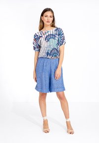 Korte mouw cropped top met een kleurrijk pauwenveerprint en verticale strepen. Gecombineerd met lichtblauwe linnen shorts, met een losse pasvorm.