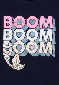 Marinblå t-shirt med färgglad text "BOOM". Texten inkluderar rosa, vit och glittrande design med en sjöjungfrusvansgrafik längst ner.