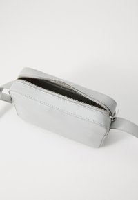 Pochette in pelle grigia di forma rettangolare, con chiusura a zip e tracolla attaccata. Texture liscia con dettagli di cucitura visibili.