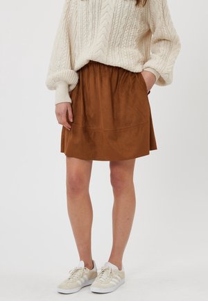 Mini-jupe en faux suède marron avec une taille élastique, assortie à un pull en maille crème et des baskets beiges.