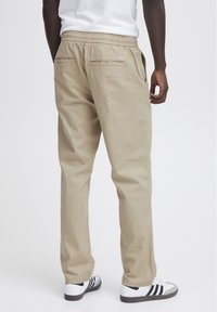 Pantaloni in cotone beige con vita elastica, dotati di due tasche posteriori e design a gamba dritta. Abbinati a sneaker bianche e nere.