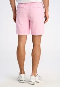 Shorts de pana rosa con una cinturilla elástica, que presentan una superficie texturizada y dos bolsillos traseros. Combinados con zapatillas deportivas grises claras.