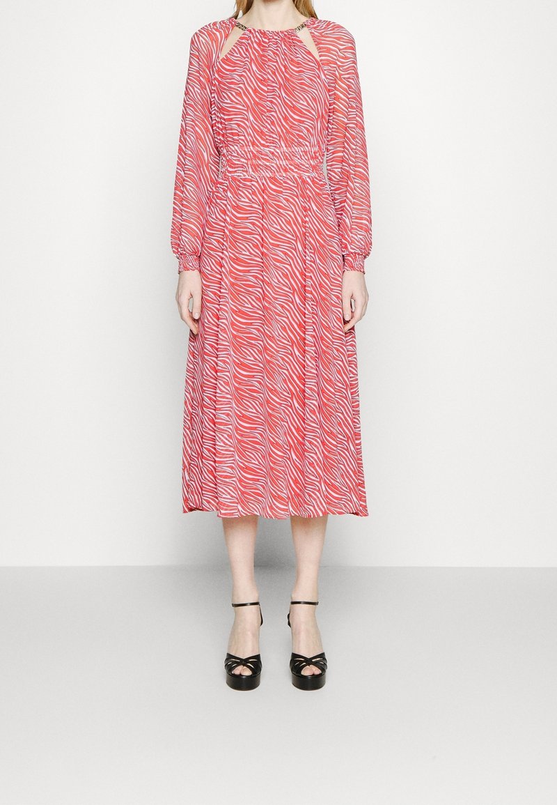 Robe midi rouge avec des rayures blanches en zèbre, manches longues, corsage froncé, décolleté en trou de serrure et chaussures à plateforme noires à lanières.