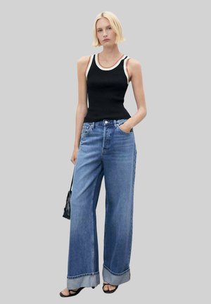 Black ribbed tank top with white trim, paired with loose blue denim jeans featuring a wide leg and cuffed hems. Model holds a small black bag.