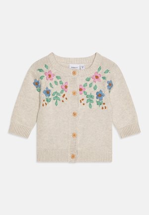 Hellcremefarbene gestrickte Babystrickjacke mit Holzknöpfen und bestickten rosa und blauen Blumen mit grünen Blättern über der Brust und den Schultern.