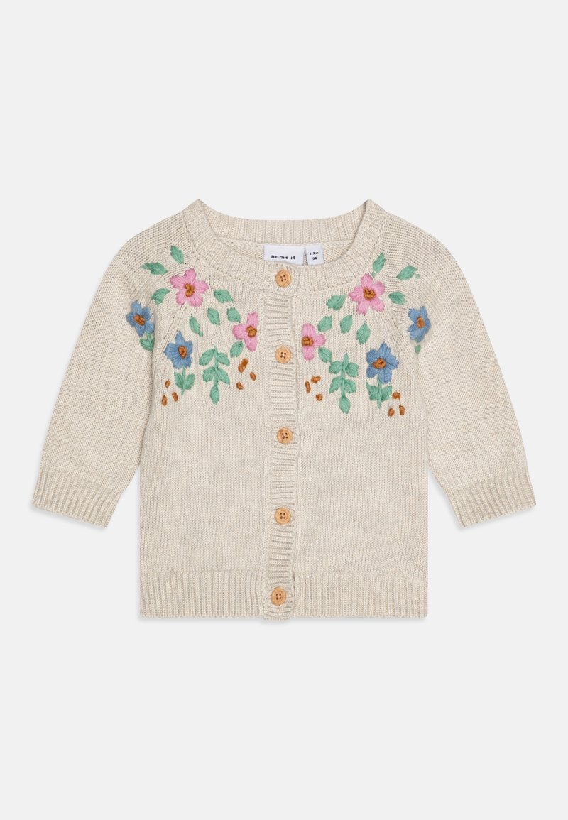 Cardigan pour bébé tricoté couleur crème avec des boutons en bois et des fleurs brodées roses et bleues avec des feuilles vertes sur la poitrine et les épaules.