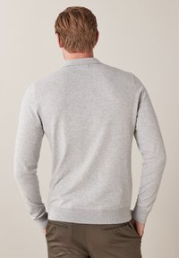 Harmaa neulepaita, jossa pitkät hihat, resorit hihoissa ja helmassa. Siinä on klassinen kaulus ja sileä pinta. Takaa näkyvät saumat ja istuvuus.