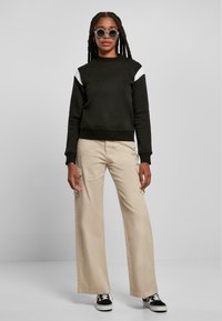 Czarna bluza z białymi akcentami na ramionach, luźne beżowe spodnie i czarne sneakersy. Model nosi okrągłe, ozdobne okulary przeciwsłoneczne.