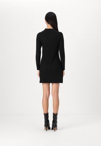 Vestido preto de malha canelada com mangas longas e barra rendada, combinado com botas de salto alto pretas até ao joelho. Design minimalista, silhueta ajustada.