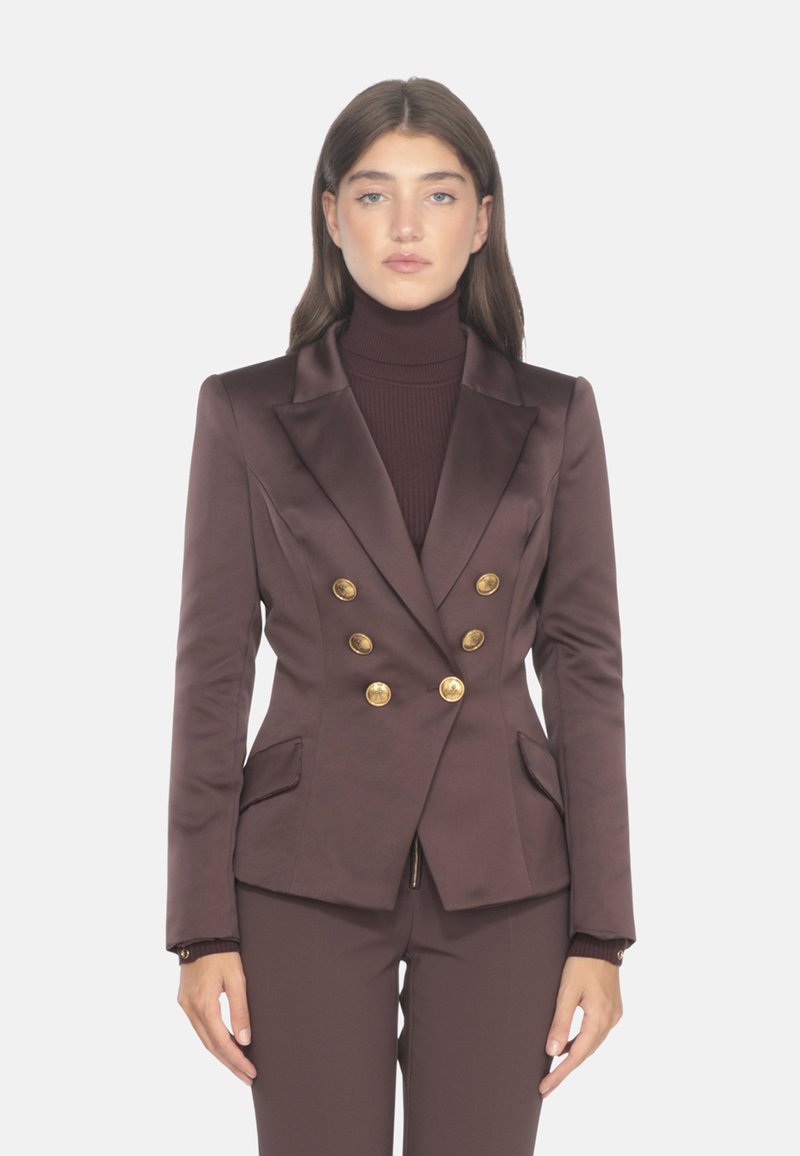 Blazer marrone doppiopetto in tessuto satinato, con bottoni dorati, rever a punta e due tasche frontali. Abbinato a un dolcevita a coste.