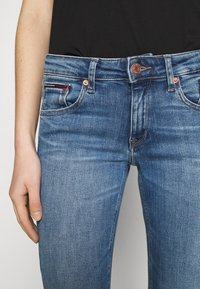 Jeans de mezclilla en azul medio, que cuentan con un clásico diseño de cinco bolsillos, remaches de cobre y un sutil desgaste en los paneles frontales.