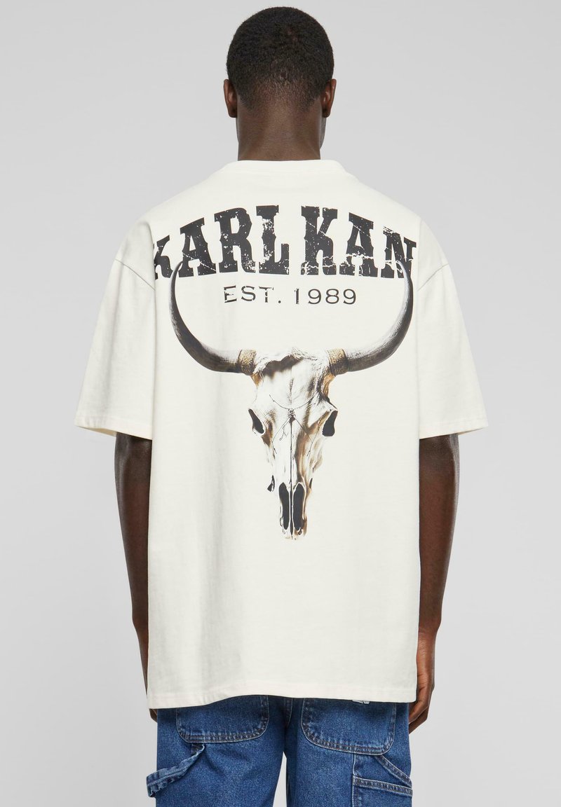 Krämfärgad t-shirt med kort ärm som har en stor grafisk design av en tjurhornskalle och texten "KARL KAN EST. 1989" i sliten svart bokstavsform.