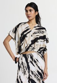 Una giovane donna con capelli lunghi e scuri indossa una maglietta larga a righe bianche e nere e pantaloni abbinati con coulisse, posando con una mano sui fianchi.