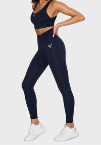 Mörkblå träningsoutfit bestående av en figurnära crop top och höga leggings, båda tillverkade av ett smidigt, stretchat material med logotypdetaljer.