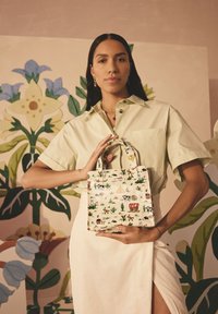 Mini tote bag lavet af et kanvaslignende materiale, med farverige illustrerede mønstre af dyr og planter. Håndtagene er syet sikkert fast.