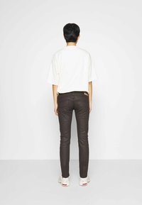 T-shirt blanc oversize à manches courtes, associé à un jean marron foncé ajusté. Vue de dos montrant un design simple et une silhouette décontractée.