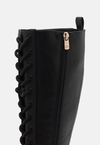 Svart syntetiskt läder knähög stövel med sidodragkedja, utrustad med svarta snören och runda öljetter. Slät textur, minimala hårdvaruaccenter.