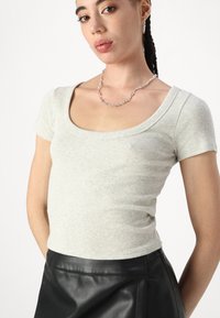 Top de manga corta de color gris claro con un escote redondeado, combinado con una falda de cuero negra. Accesorios con un collar de cadena de plata.