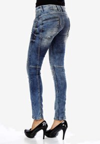 Jean skinny en denim bleu avec un délavage, des coutures détaillées et plusieurs poches, associés à des escarpins noirs brillants.