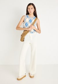 Svetre brez rokavov v sivi barvi z argyle vzorcem v modrih in belih rombih, kombiniran z kremnimi širokimi hlačami in bež platformami. Rjava torbica preko telesa.