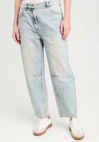Lysblå, højtaljede jeans med lige ben design, der har slidte områder og synlige syninger. Parret med hvide sneakers.