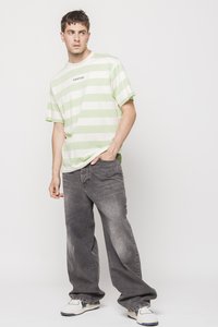 Grønn og hvit stripete t-skjorte med en logo, parret med grå løstsittende jeans og joggesko, mot en enkel bakgrunn.
