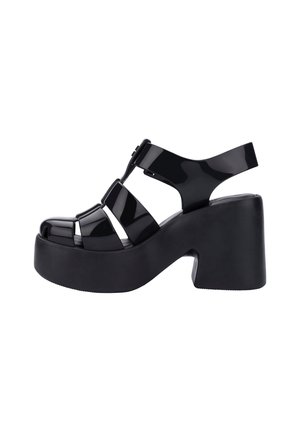 Sandalias de plataforma de charol negro con tacón grueso, diseño de punta abierta y detalles de tiras entrecruzadas.