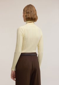 Jasnożółty, prążkowany sweter z golfem i długimi rękawami, o dopasowanym kroju, zestawiony z brązowymi spodniami z wysokim stanem i czarnym paskiem.