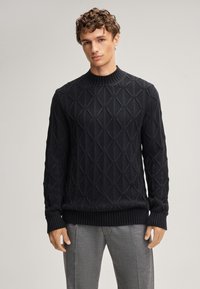 Schwarzer Strickpullover mit geometrischen Mustern, geripptem Halsausschnitt und Bündchen, weiche Textur, kombiniert mit grauen Hosen.