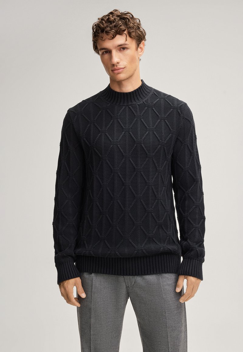 Schwarzer Strickpullover mit geometrischen Mustern, geripptem Halsausschnitt und Bündchen, weiche Textur, kombiniert mit grauen Hosen.