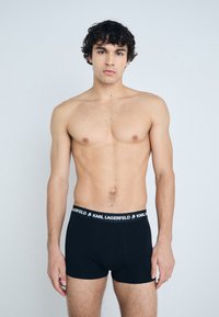Shorts de boxe noirs avec une taille élastique douce portant le logo "KARL LAGERFELD" en blanc. Tissu lisse, design ajusté, longueur mi-cuisse.