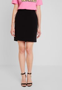 Svart figursydd kjol med en slät textur och rak nederkant, kombinerad med svarta sandaler med remmar och en rosa t-shirt med grafiskt mönster.