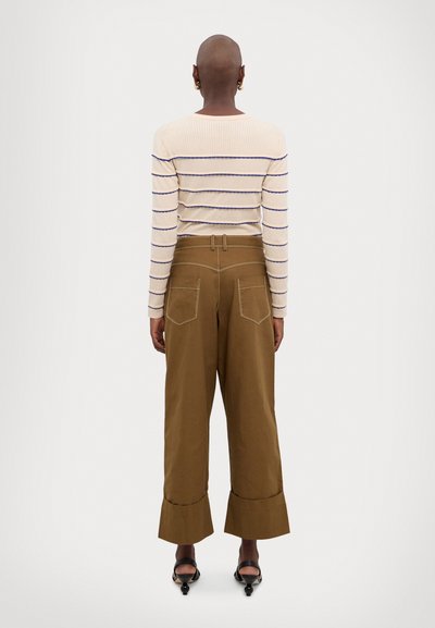 Suéter de punto a rayas en crema con líneas azules, combinado con pantalones de pierna ancha marrones que tienen puños acampanados y bolsillos traseros.