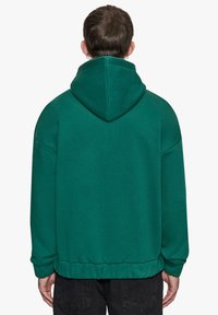Grøn oversized hættetrøje med snor i hætten, ribbede manchetter og kant. Glat tekstur, afslappet design og løs pasform.