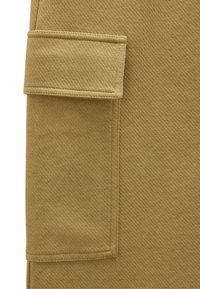 Tkanina w odcieniu brązu z widoczną dużą kieszenią z klapką z boku, wzmocnionymi szwami wzdłuż krawędzi i czystymi liniami.