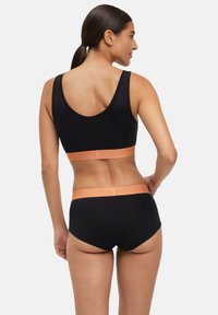 Schwarzer nahtloser Sport-BH und passende Slips mit einem kontrastierenden orangen Band. Der Stoff wirkt glatt und dehnbar, mit einem minimalistischen Design.