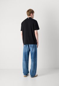 Svart T-skjorte med kort erme og rund hals, med en hvit stripete detalj på ryggen, kombinert med lyseblå, vide denimjeans.