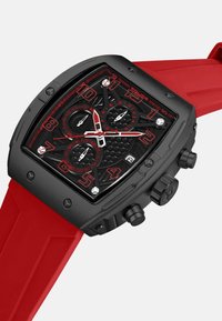 Juodas kvadratinis laikrodžio korpusas su raudonais akcentais. Juodas tekstūruotas ciferblatas su dviem subciferblatais ir dideliais skaičiais. Raudonas guminis dirželis su kampuotu dizainu.