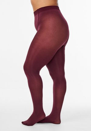 Person iført gennemsigtige bordeauxfarvede strømpebukser, stående på en hvid overflade med fødderne fladt på jorden og den ene en smule fremad.