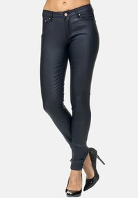 Zwarte neplederen skinny broek met vijf zakken, zichtbare stiksels en een rits. Draagt een paar zwarte hoge hakken, met een slim fit ontwerp.