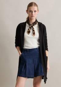 Schwarze Strickjacke, weißes geripptes Top, gemusterter Schal und dunkelblaue Jeansshorts mit Falten. Mit Taschen und lässigem Schnitt.