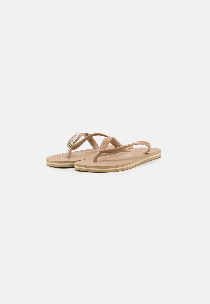 Des tongs beiges avec des brides en caoutchouc, présentant une semelle texturée, une semelle fine et un petit logo multicolore sur la bride supérieure.
