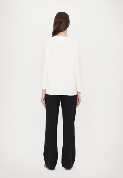 Biely sveter s reliéfnou textúrou, s okrúhlym výstrihom a dlhými rukávmi, kombinovaný s čiernymi širokými nohavicami.