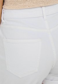 Jeans in denim bianco con una singola tasca posteriore rettangolare caratterizzata da dettagli di cucitura sottili. Il tessuto appare liscio con una leggera texture.