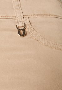 Tessuto misto cotone beige con una texture liscia, caratterizzato da cuciture visibili e da un tirante in metallo a forma di cuore.