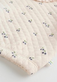Coperta trapuntata in morbido tessuto rosa, con un motivo di piccole ciliegie blu e foglie verdi. I bordi presentano una finitura texturizzata e arricciata.