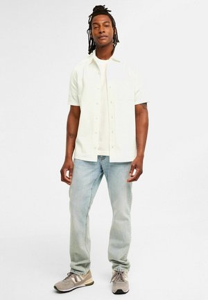 Korte mouwen, overhemd met kraag in lichtgroene, gestructureerde stof, gecombineerd met lichtblauwe jeans en grijze sneakers. Bevat een borstzakje.