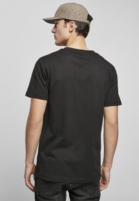 T-shirt en coton noir à manches courtes, texture lisse. Porté avec un jean foncé et une casquette de couleur claire, affichant des détails de conception minimes.