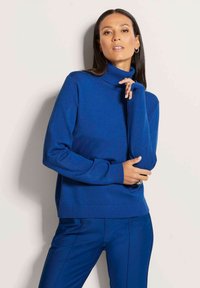 Blauer Rollkragenpullover aus weichem Stoff, mit körpernahem Schnitt, gerippten Bündchen und Saum. Kombiniert mit passenden blauen Hosen.
