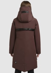 Brun polstret parka med hætte, der har et sort logo-bånd på tværs af ryggen og trykknaplukning i sømmen. Glat tekstur, knælang.
